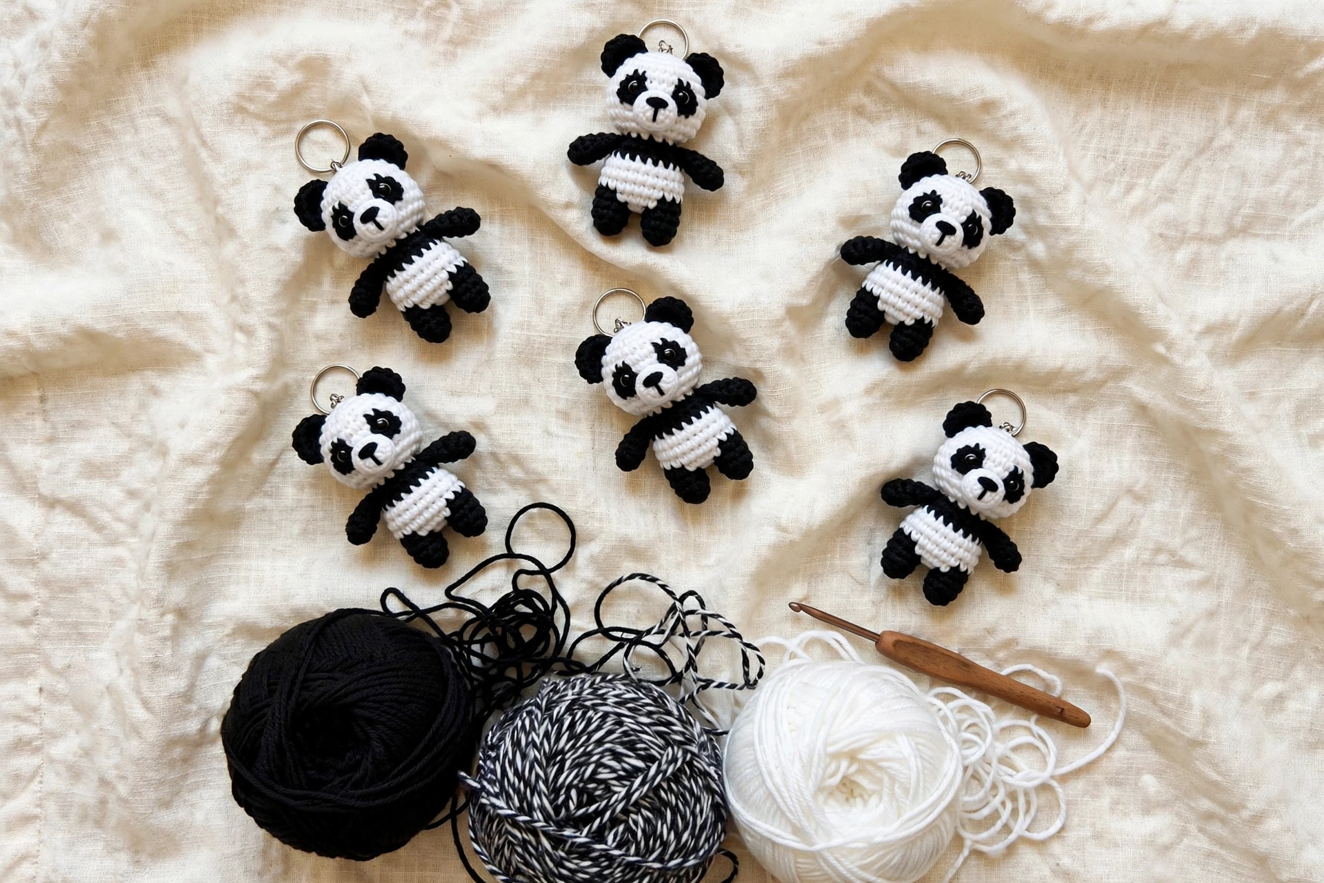 Six mini crochet panda keychains with yarn balls and a crochet hook on linen